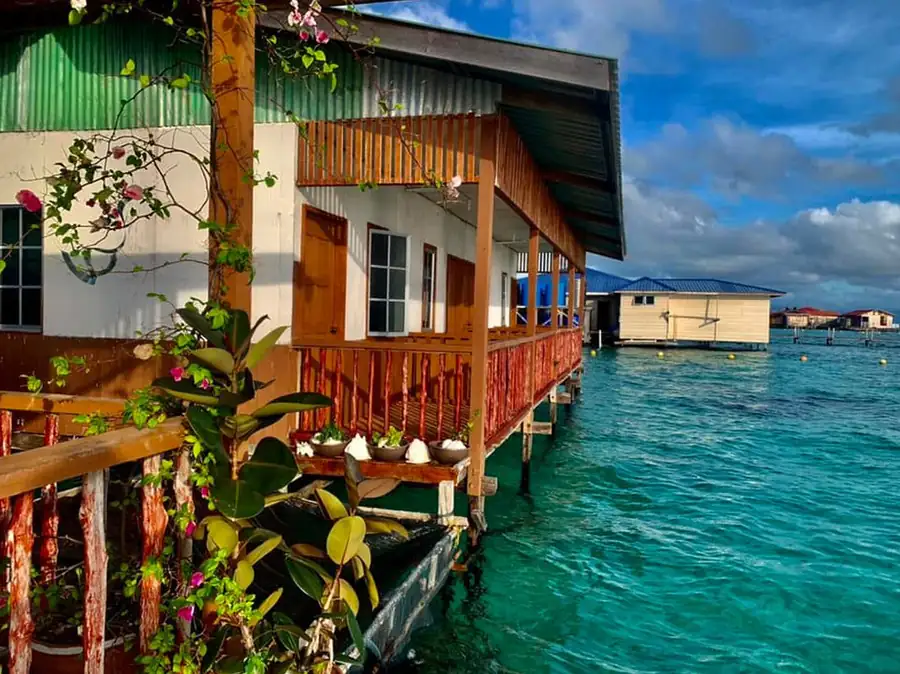 A rustic wooden water chalet featuring flower-lined railings and timber walkways over clear turquoise water at Bihing Angan Water Chalet.