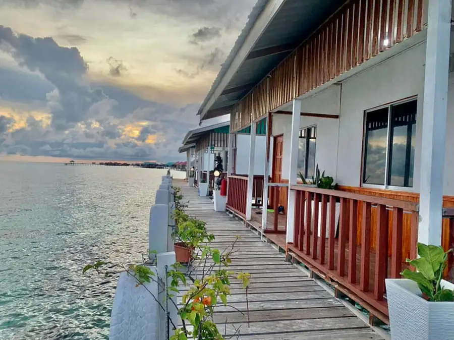 A row of overwater bungalows in a traditional Sabah style featuring wooden railings and sloped metal roofs at Bihing Angan Water Chalet.